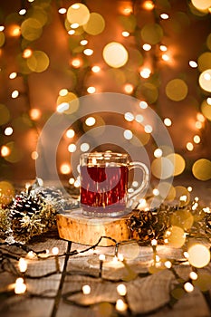 Holiday scene of fruit tea in a glass mug with decoration and bokeh lights on a wooden table and christmas lights