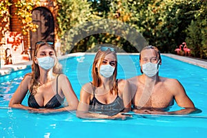 A holiday at sea and protection from viruses. A group of young people pose in a pool with medical masks on their faces. The