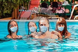 A holiday at sea and protection from viruses. A group of young people swim in a pool with medical masks on their faces. The