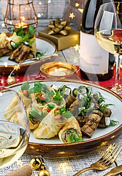 Holiday snacks with zucchini and eggplant rolls on wooden table served with plates, glasses, bottle of wine, candles, festive