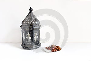 Holiday still life composition. Plate with date fruits and ornamental dark Moroccan, Arabic lantern on the white table