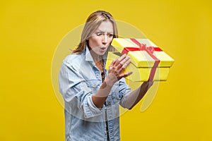 Holiday surprise. Portrait of astonished curious woman in denim shirt looking inside gift box. studio shot  on yellow