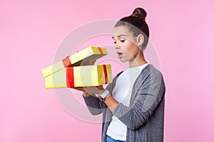 Holiday surprise. Portrait of curious teenage brunette girl looking inside gift box. isolated on pink background photo