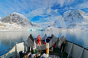 Holiday travel in Arctic, Svalbard, Norway. People on the boat. Winter mountain with snow, blue glacier ice with sea in the foregr