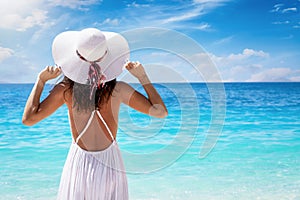 Holiday travel concept with a woman in white dress and hat looking at turquoise colored sea