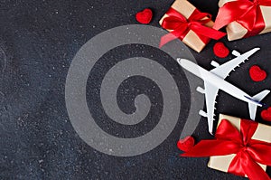 Holiday Travel Planning. Travel concept. Airplane model, gift boxes and red hearts on dark background
