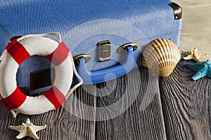 Holiday travel suitcase, lifebuoy and shells on wooden table