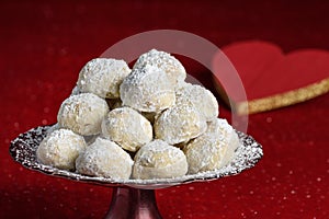 Holiday treat, Russian Teacakes stacked on a red cake plate, on a red velvet tablecloth, red heart for Valentines in background