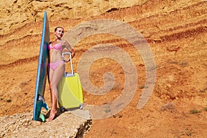 Holiday trip, tourism and relax idea, copy space. Pretty woman with surfboard and suitcase. Sunny weather for sunbath