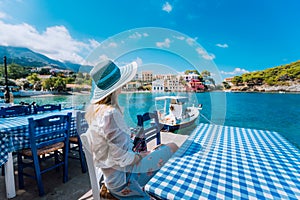 Holiday vacation. Woman in cafe enjoying time in Assos village in front of emerald bay of Mediterranean sea white boat