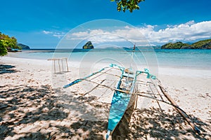 Holiday vibes. Traditional fishermen banca boat on sandy empty tropical beach. Blue ocean lagoon in background. El Nido