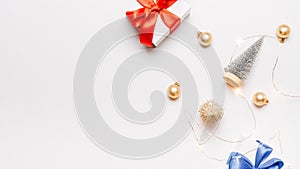 Holiday winter background. White gift box with red ribbon, New Year balls and sparkling lights garland in Christmas