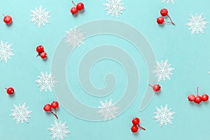 Holiday winter background. White snowflakes, red berry in Christmas composition on pastel blue background for greeting card. Xmas