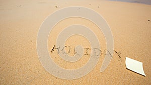 Holiday written in the sand at the beach with post it