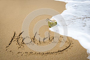 Holiday written in sand on a beach.