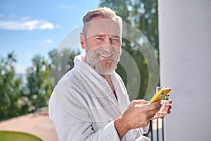 Holidaymaker with a beverage and a smartphone on the balcony