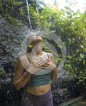 Holidays adventure lifestyle portrait - young beautiful and happy woman taking natural shower from waterfall in the jungle