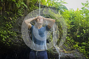 Holidays adventure lifestyle portrait - young cool and happy man taking natural shower from waterfall in the jungle enjoying the