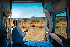 Holidays in Australia. Woman having a coffee at the back side of a caravan. Casual clothes, cup on her hands. Morning time.