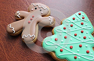 Holidays Background With Gingerbread Man And Pine Tree Cookies With Colored Icing On Leather Surface