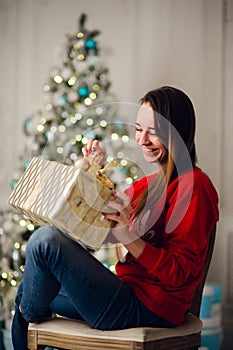 Holidays, celebration and people concept - smiling woman wearing red sweather and jeans holding gold gift box over