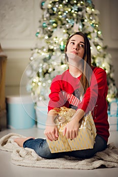 Holidays, celebration and people concept - smiling woman wearing red sweather and jeans holding gold gift box over