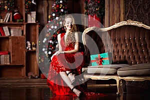 Holidays, celebration and people concept - young smiling woman in elegant red dress over christmas interior background