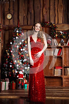 Holidays, celebration and people concept - young smiling woman in elegant red dress over christmas interior background