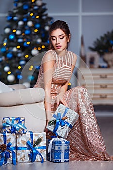 Holidays, celebration and people concept - young woman in elegant dress over christmas interior background