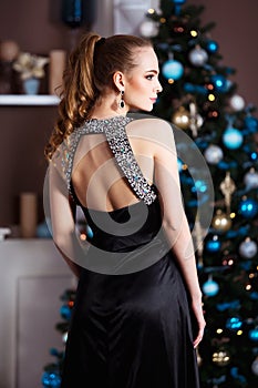 Holidays, celebration and people concept - young woman in elegant dress over christmas interior background.