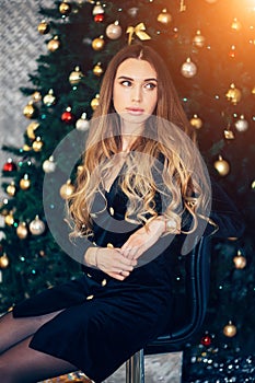 Holidays, celebration and people concept - young woman in elegant dress over christmas interior background. Girl in black dress