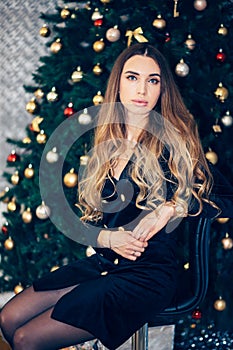 Holidays, celebration and people concept - young woman in elegant dress over christmas interior background. Girl in black dress ne