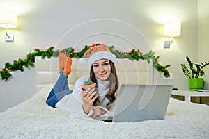 Holidays christmas interior winter concept. young woman in cozy bedroom with laptop computer lying on bed at home. New