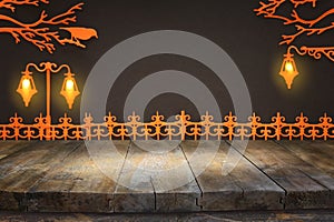 Holidays concept of Halloween. Empty rustic table in front of vintage fence and street lamp in the park over black background.