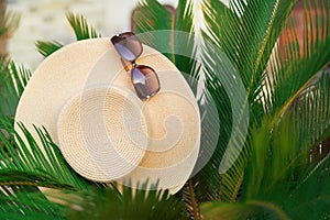 Holidays concept layout. Straw hat on the pubble beach under palm tree leaves. Vacation accesories