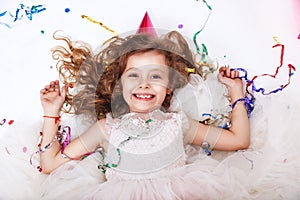 Holidays concept. Little funny girl lying in multicolored confetti on birthday party