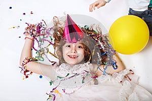 Holidays concept. Little funny girl lying in multicolored confetti on birthday party