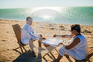 Holidays, family aconcept - Portrait of elderly couple standing together with glasses of wine and embracing on the beach.