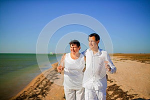 Holidays, family aconcept - Portrait of elderly couple standing together with glasses of wine and embracing on the beach.