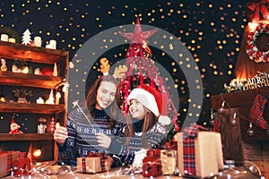 Holidays, family and people concept. Happy mother and little girl in santa helper hat with sparklers in hands, gift