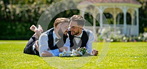 Holidays, Festivals, and Events lgbt concept. Gay marriage couple laying on grass on wedding day.