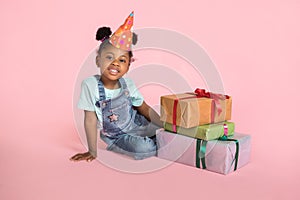 Holidays, happy childhood. Portrait of a satisfied cute little african girl in birthday party hat, sitting on the floor