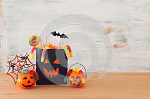 Holidays image of Halloween. Pumpkins, bats, treats, paper gift bag over wooden table