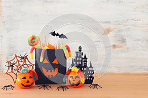 Holidays image of Halloween. Pumpkins, bats, treats, paper gift bag over wooden table