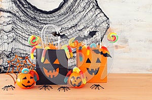 Holidays image of Halloween. Pumpkins, bats, treats, paper gift bag over wooden table