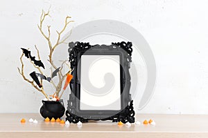 holidays image of Halloween. witcher cauldron, broom, bare trees, photo frame over white wooden table