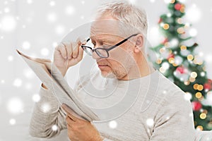 Senior man in glasses reading newspaper at home