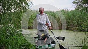 holidays on lake, grandpa standing on a boat rowing an oar along green muddy river with his little grandchild