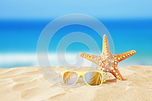 Holidays. sand beach, sunglasses and starfish in front of summer sea background with copy space