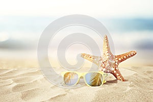 Holidays. sand beach, sunglasses and starfish in front of summer sea background with copy space